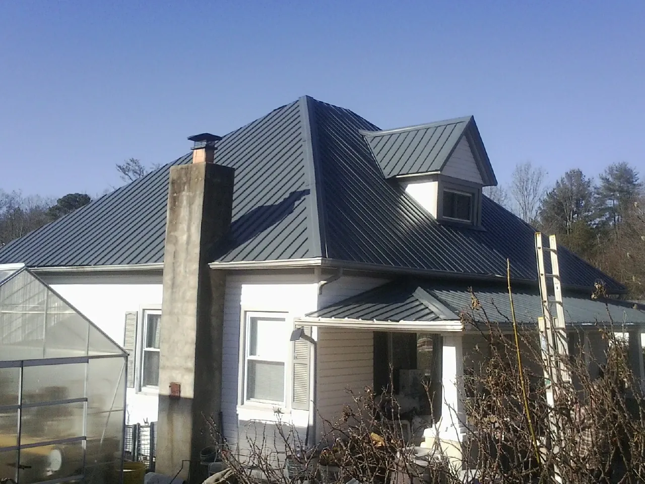 Dark blue standing seam metal roof on a white farmhouse with dormer — Slate & Tile Roof Repair by Roofing Brothers in Charlottesville