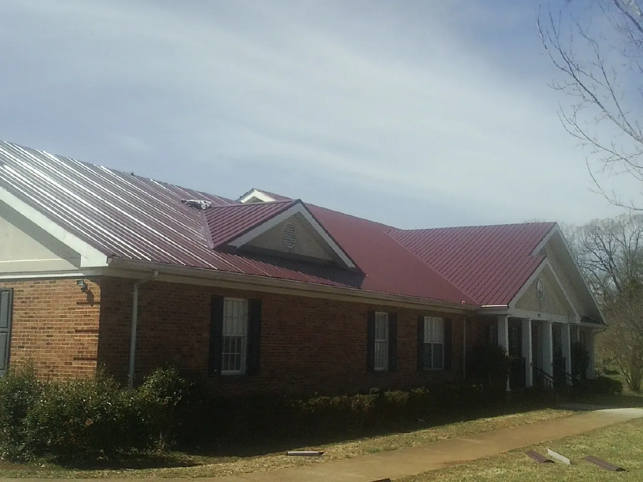 Red metal roof with gabled entries on a long brick building, from a Hail Damage Roof Repair job in Charlottesville