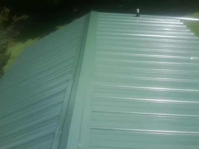 New green metal panels meeting at the ridge of a roof — Flat Roof Repair work by our crew in Charlottesville