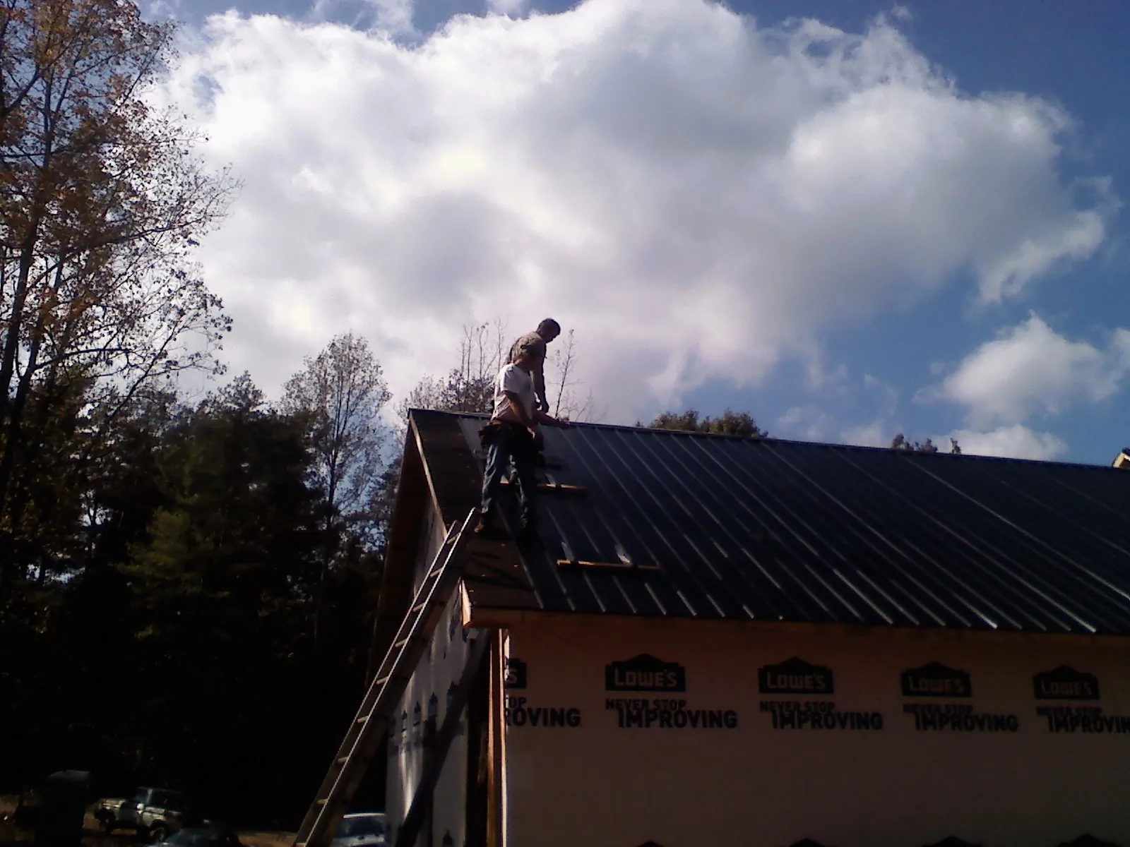 Roofer fastening dark metal panels high against a cloudy sky, from a Roof Inspection job in Charlottesville