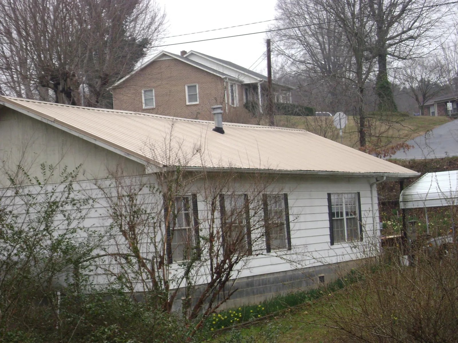 Tan metal roof on a white sided house set into a hillside — Commercial Roofing by Roofing Brothers in Charlottesville