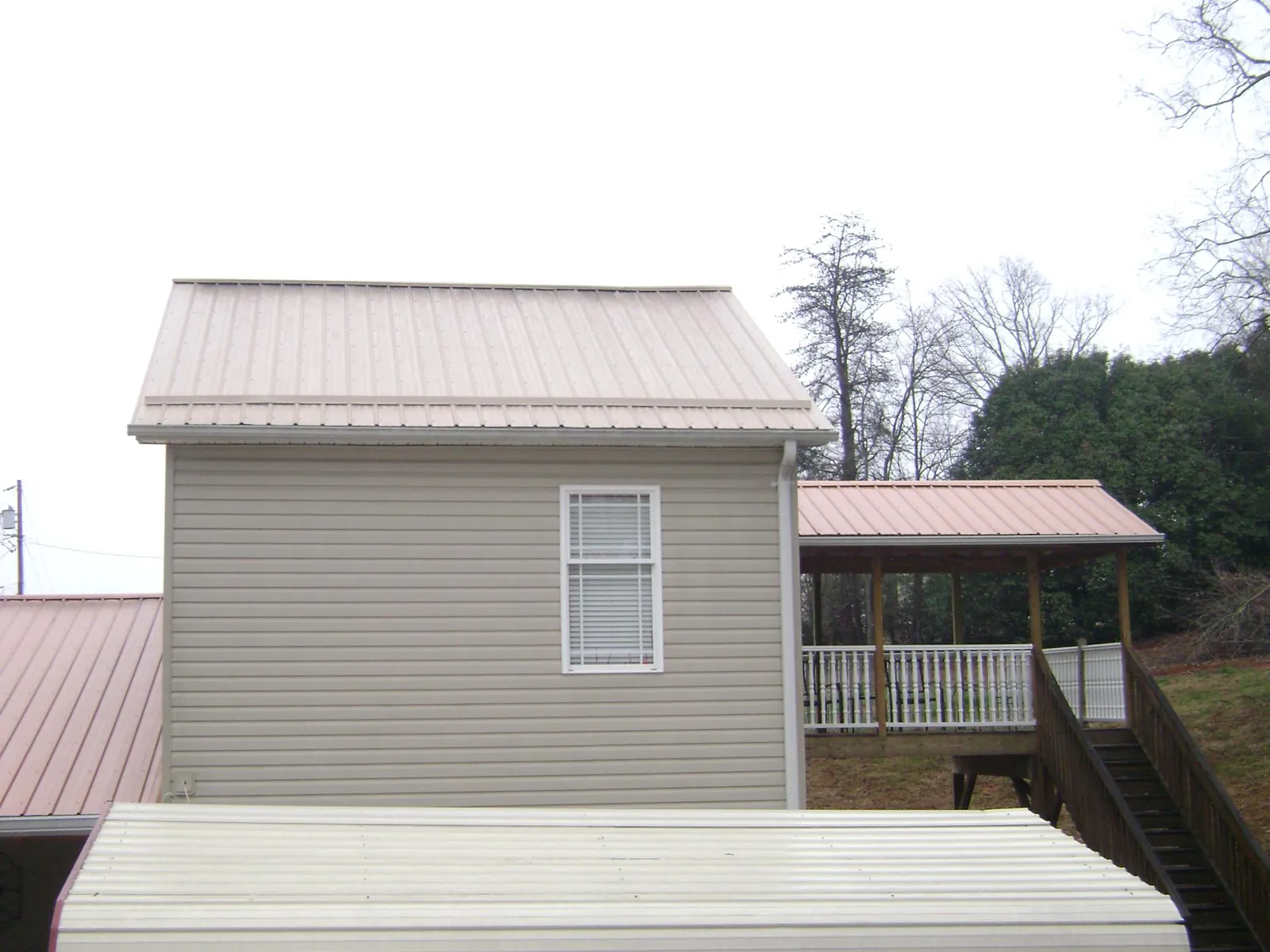 Tan metal roofs on a two story addition and attached porch, from a Roof Replacement job in Charlottesville